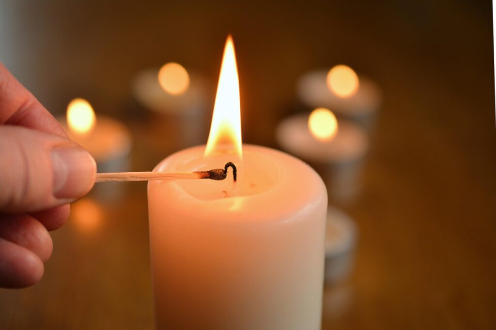 Lighting a single candle with candles in the background.